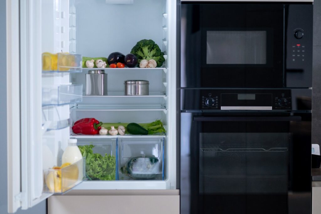 Un frigo ouvert avec des divers aliments placé près d'un micro-onde