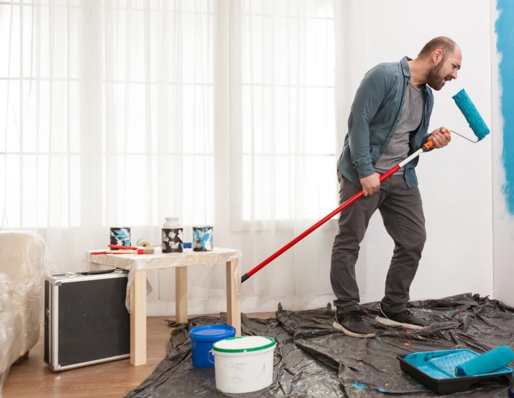 Un homme qui tient un rouleau de peinture en peint le mur en bleu