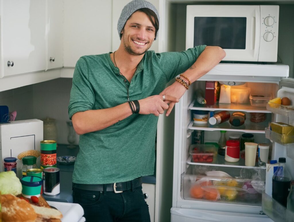 Un homme souriant qui se tient debout près du frigo ouvert avec un micro-onde placé dessus