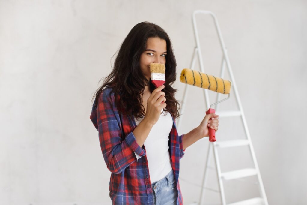 Une jeune femme qui tient un pinceau et un rouleau de peinture