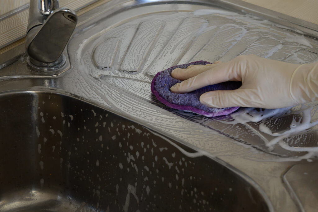 Une main gantée nettoyant un évier de cuisine