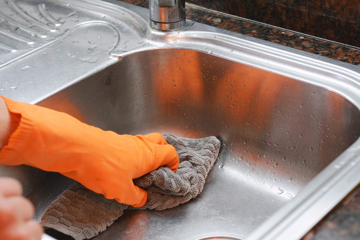 Une personne portant un gant orange et nettoie l'évier inox