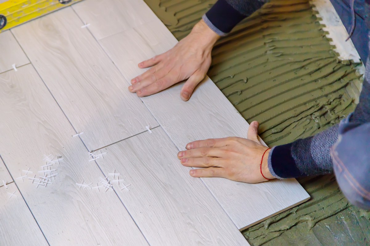 Mains posant du carrelage sur du ciment