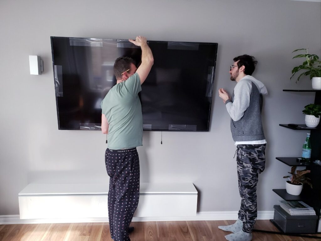 Des hommes accrochant une grande télévision sur le mur