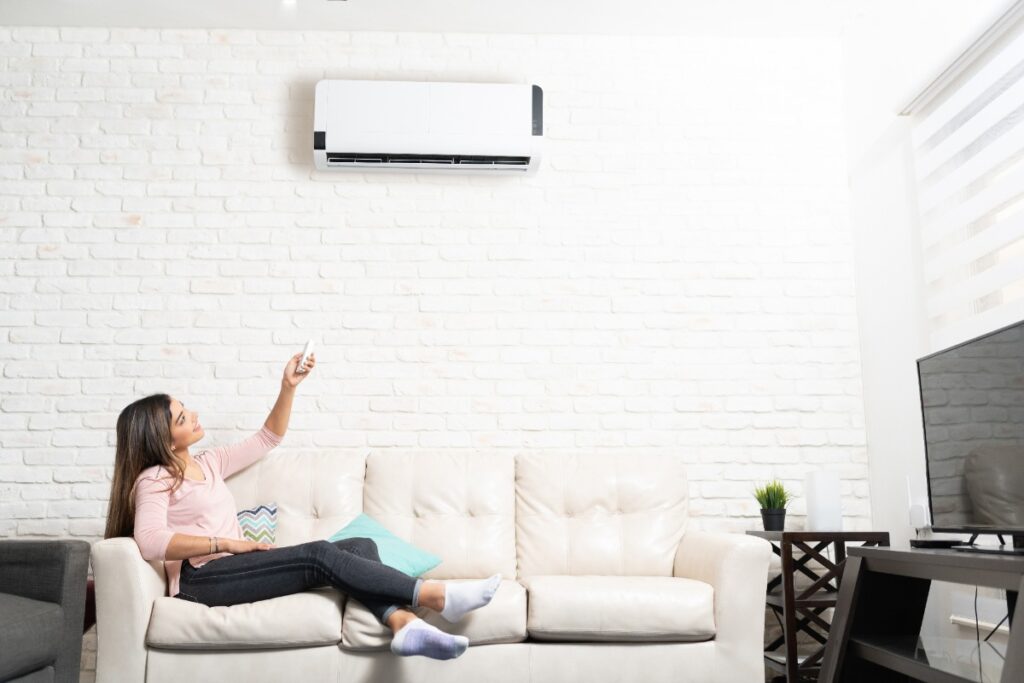 Une femme assise sur un canapé en réglant le climatiseur